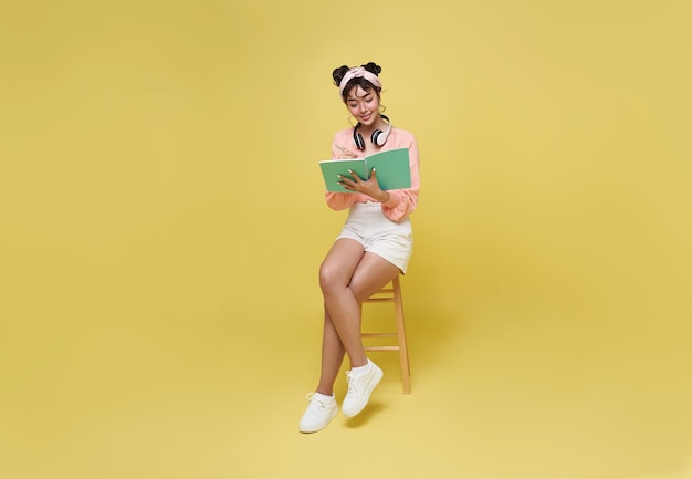 Young woman Asian girl making notes sitting on chair isolate on bright yellow background