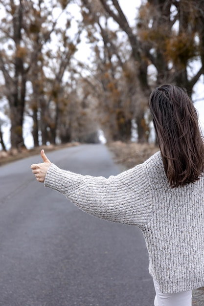 アスファルト道路ヒッチハイクの概念の若い女性