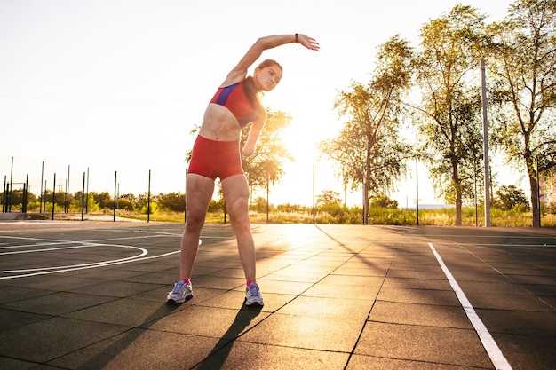 Young woman athlete with an amputated arm and burns on her body doing tilt exercise on the sports field Outdoor training at sunset