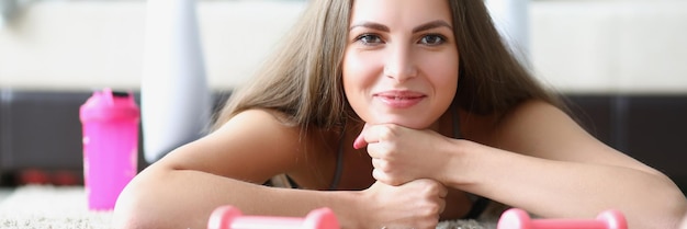 Young woman athlete with dumbbells in her hands lying on floor at home