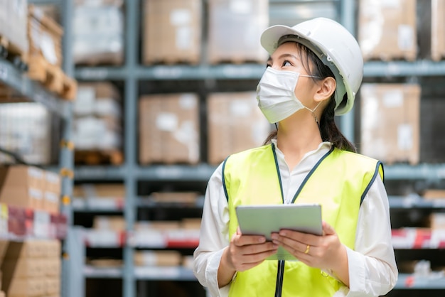 Young woman auditor or trainee staff wears mask working during the COVID pandemic in store warehouse