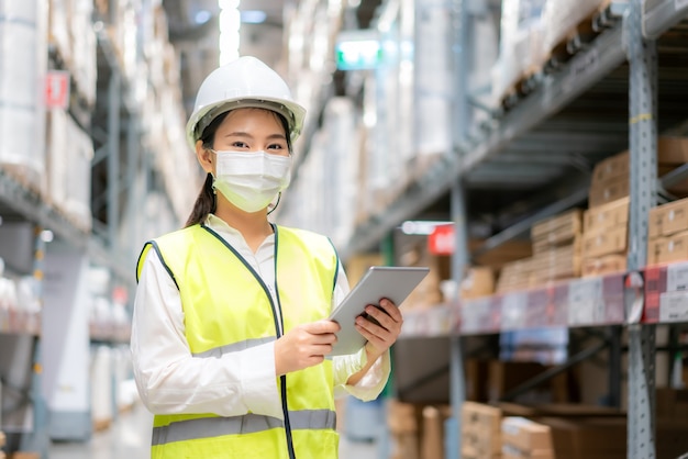 Young woman auditor or trainee staff wears mask working during the COVID pandemic in store warehouse