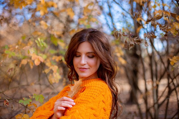 Una giovane donna in un parco autunnale con un maglione arancione