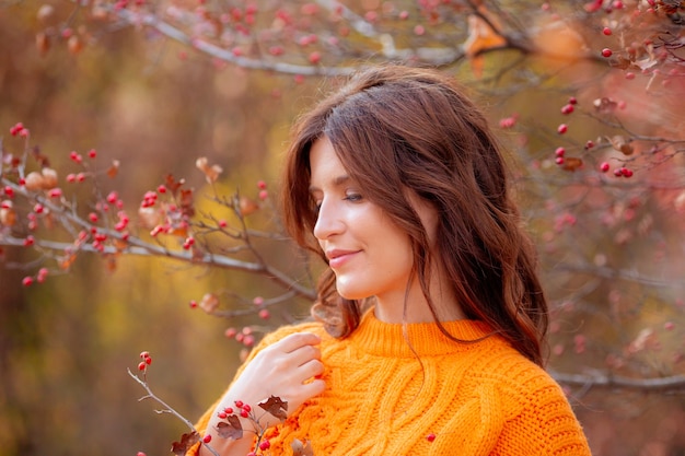 オレンジ色のセーターの秋の公園で若い女性