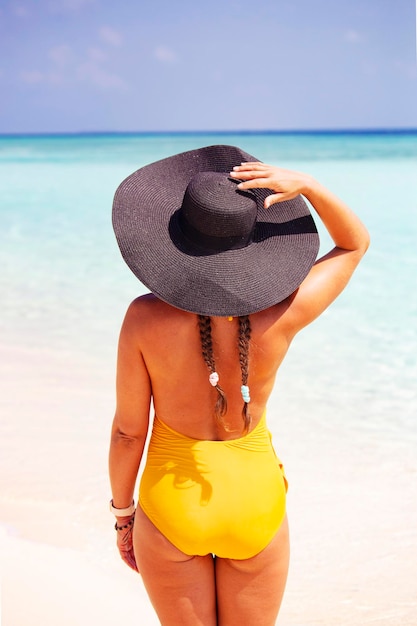 Young woman back view unrecognized wearing hat and swimming suite on the tropical beach, Maldives