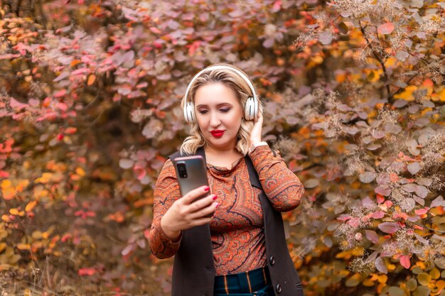 音楽を聴いているヘッドフォンで秋の公園の背景に若い女性