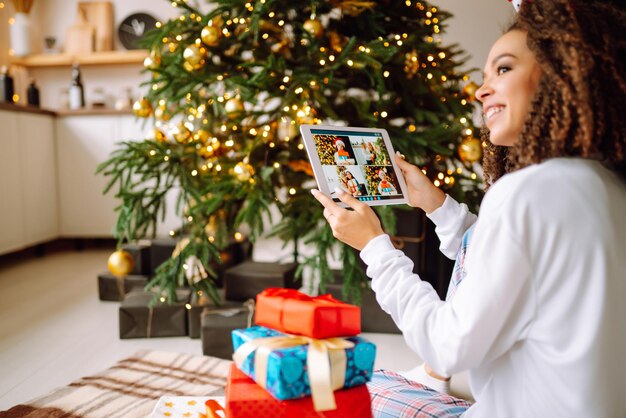 タブレットでギフトとクリスマス ツリーの背景に若い女性がビデオ通話またはビデオ チャットをしています。