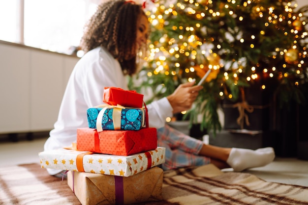 A young woman on background of Christmas tree with gifts with tablet has video call or video chat