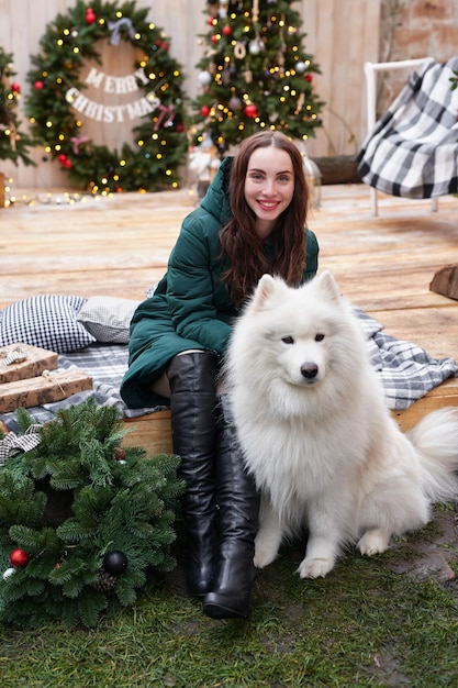 新年の白いサモエド犬屋外庭の装飾とクリスマス ツリーの背景に若い女性