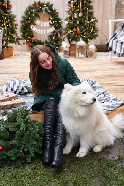 新年の白いサモエド犬屋外庭の装飾とクリスマス ツリーの背景に若い女性