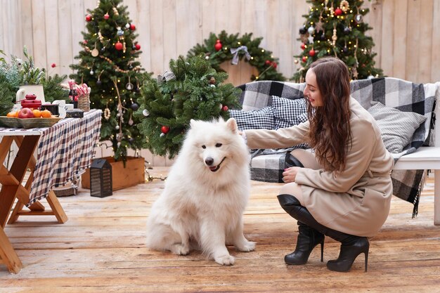 新年の白いサモエド犬屋外庭の装飾とクリスマス ツリーの背景に若い女性