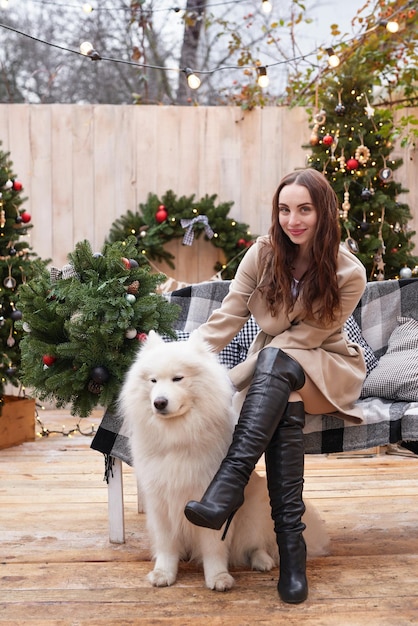 新年の白いサモエド犬屋外庭の装飾とクリスマス ツリーの背景に若い女性