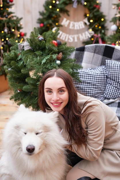 新年の白いサモエド犬屋外庭の装飾とクリスマス ツリーの背景に若い女性
