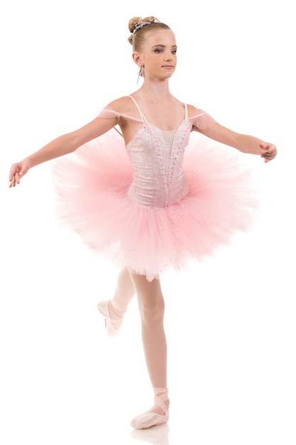 Young woman ballerina in white tutu dancing on pointe with arms overhead in the studio against a dark background