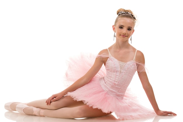 Photo young woman ballerina in white tutu dancing on pointe with arms overhead in the studio against a dark background