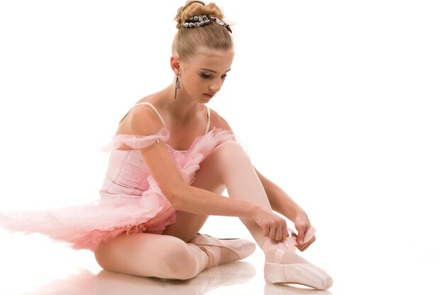 Young woman ballerina in white tutu dancing on pointe with arms overhead in the studio against a dark background