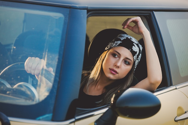 Young woman in a bandana drives a car on a rural road
