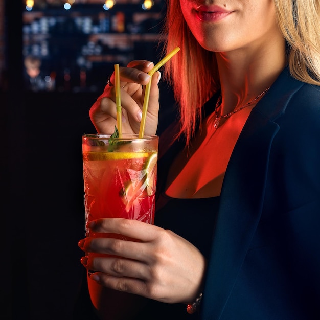 Молодая женщина в баре или клубе развлекается на заднем плане своего бара, фокусируясь на стакане мохито, который она держит в руке