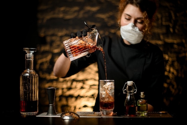 Young woman at bar pours cold cocktail into glass