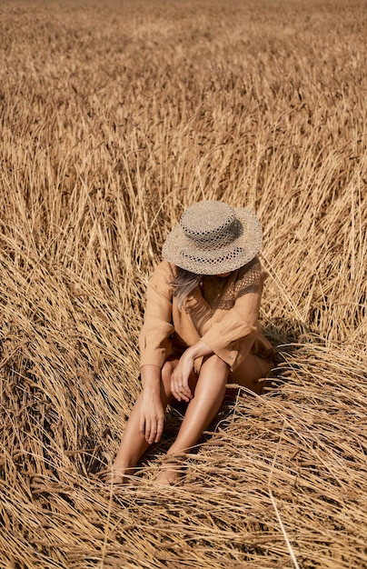 Young woman barefoot in linen clothes and a hat on a background of dry grass romantic girl in a hat