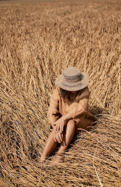 Young woman barefoot in linen clothes and a hat on a background of dry grass romantic girl in a hat