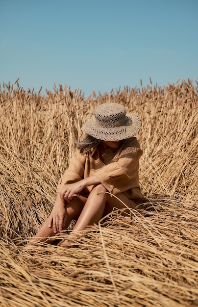 Young woman barefoot in linen clothes and a hat on a background of dry grass romantic girl in a hat