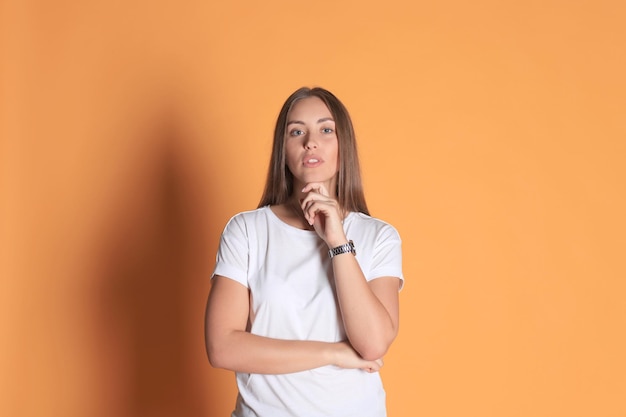 Young woman in basic clothing smiling and pointing finger at copyspace isolated on yellow background.