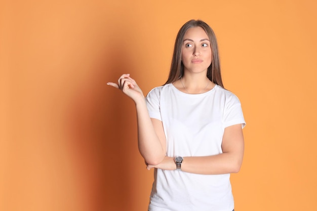 Young woman in basic clothing smiling and pointing finger at copyspace isolated on yellow background.