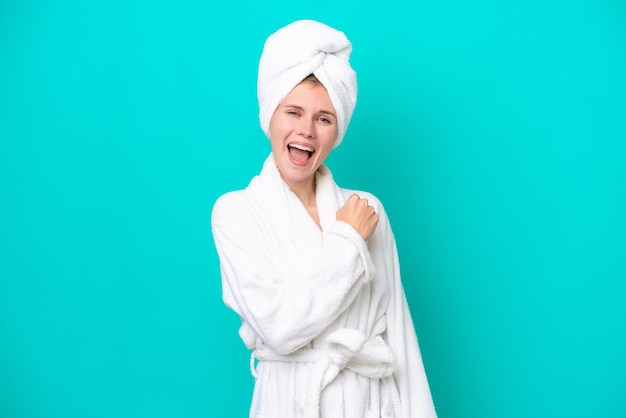 Young woman in a bathrobe isolated on blue background celebrating a victory