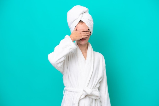 Young woman in a bathrobe isolated on blue background covering eyes by hands Do not want to see something