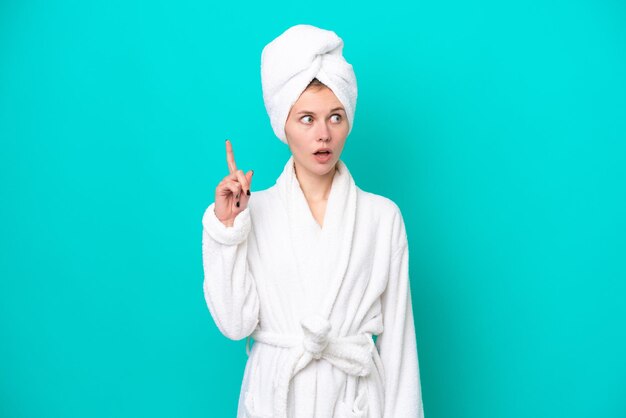 Young woman in a bathrobe isolated on blue background thinking an idea pointing the finger up