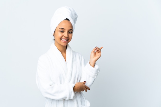 Young woman in bathrobe over isolated white happy and pointing up