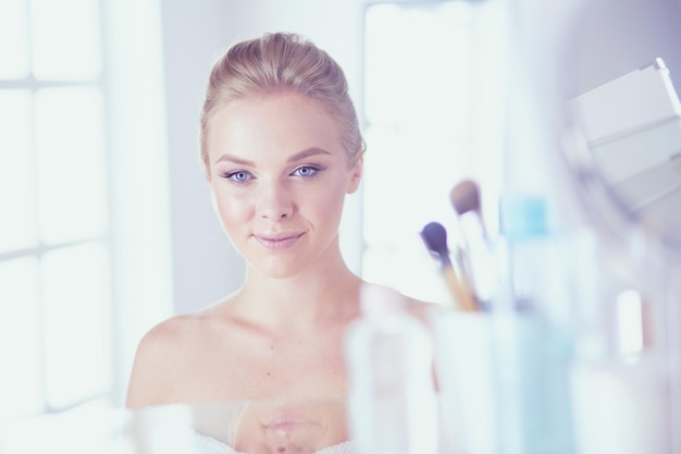 Young woman in bathrobe looking in bathroom mirror