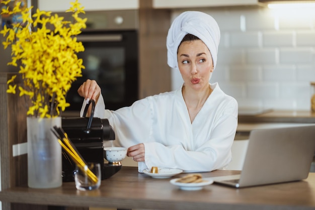 Young woman in bathrobe making coffee with a coffee machine in her kitchen at the morning