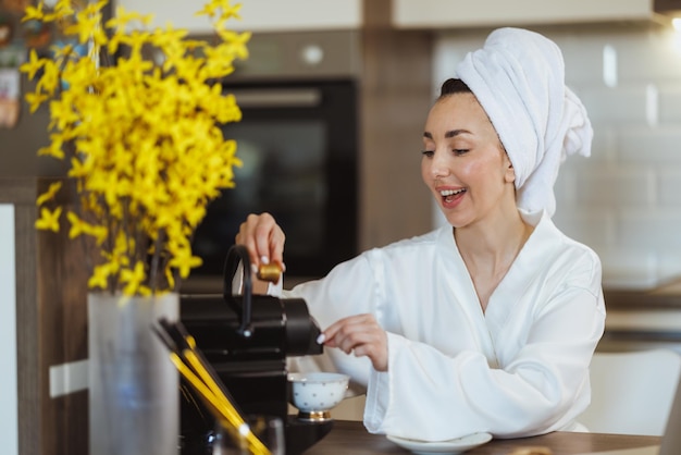 Young woman in bathrobe making coffee with a coffee machine in her kitchen at the morning.