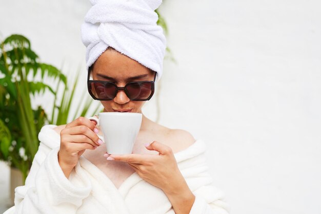 バスローブを着て頭にタオルを乗せた若い女性が、クロワッサンとイチゴの入った朝食コーヒーを飲みながらリゾートでの休暇を楽しんでいる