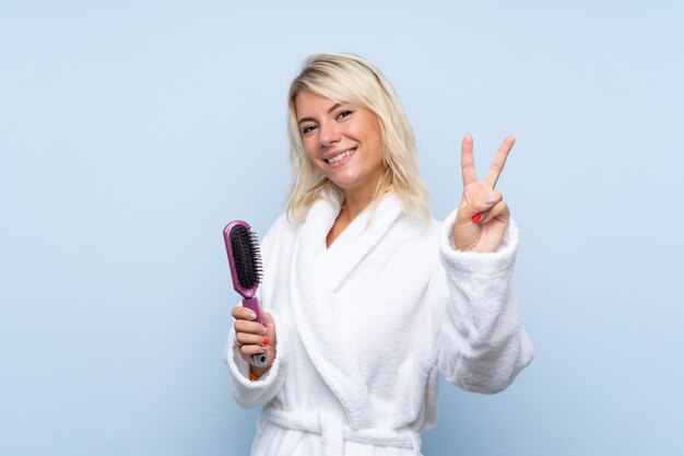 Young woman in a bathrobe with hair comb smiling and showing victory sign