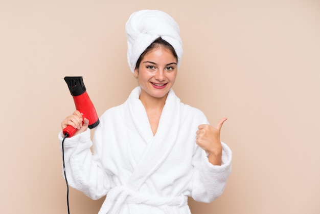 Young woman in a bathrobe with hairdryer over isolated wall with thumbs up because something good has happened