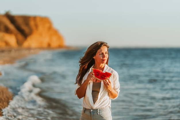 海沿いのビーチで、日没時にスイカを食べる若い女性静かな夏の夜