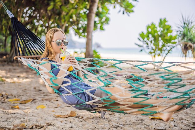 Young woman on the beach in a hammock with a drink