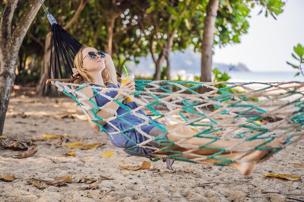 Young woman on the beach in a hammock with a drink