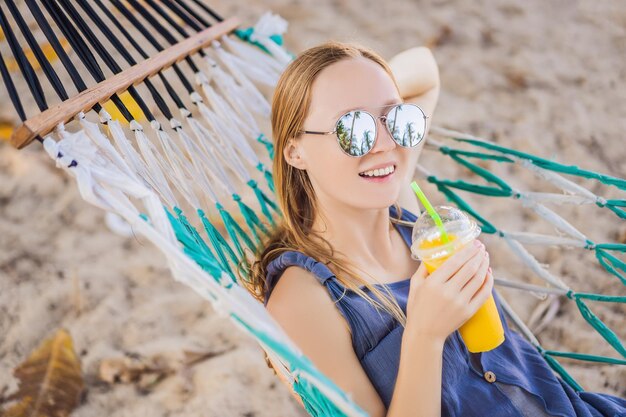 Young woman on the beach in a hammock with a drink