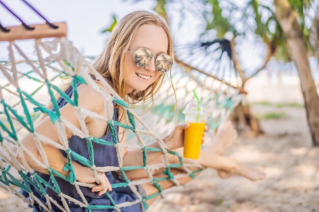 Young woman on the beach in a hammock with a drink