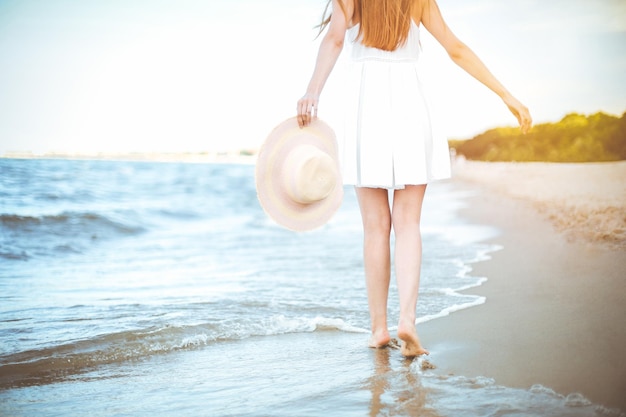 Young woman on a beach holding a white hat. Legs close up.