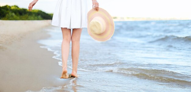 Young woman on a beach holding a white hat. Legs close up