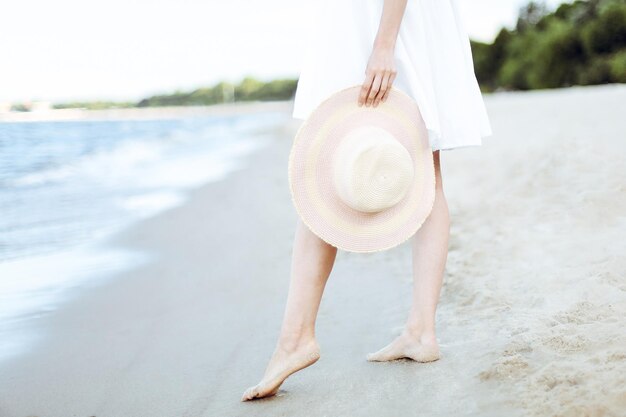 Photo young woman on a beach holding a white hat legs close up