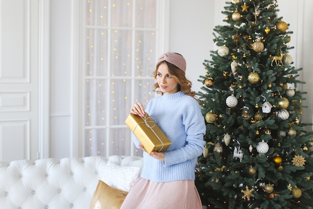 A young woman beauty with a gift in her hands stands by the tree