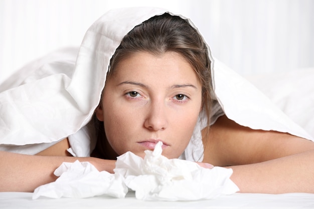 A young woman in bed having flu over white background