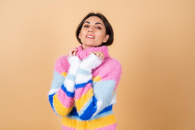 Young woman on beige in a bright multicolored cozy knitted sweater cute smiling