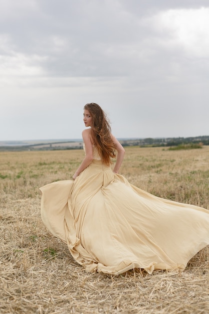 Young woman in a beige dress in wheat field